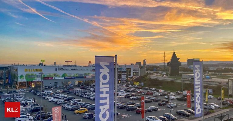 Ein Parkplatz mit vielen geparkten Autos unter einem schönen Sonnenuntergang mit einem großen Gebäude im Hintergrund.