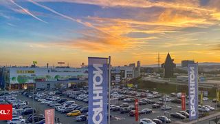 Ein Parkplatz mit vielen geparkten Autos unter einem schönen Sonnenuntergang mit einem großen Gebäude im Hintergrund.