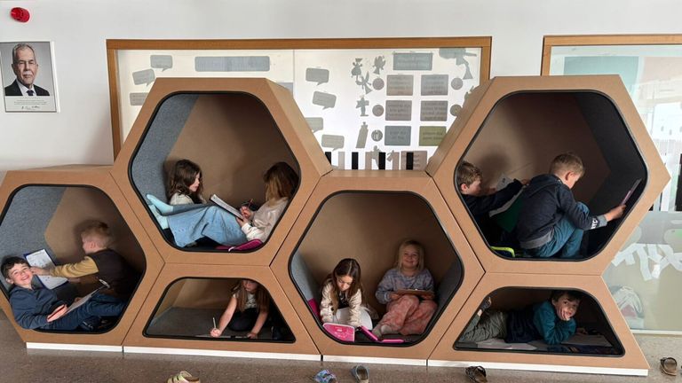 Eine Gruppe von Kindern sitzt in einer sechseckigen Leseecke aus Pappe. Sie lesen Bücher und schreiben.