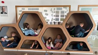 Eine Gruppe von Kindern sitzt in einer sechseckigen Leseecke aus Pappe. Sie lesen Bücher und schreiben.