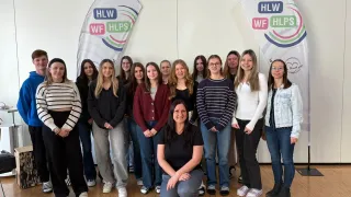 Eine Gruppe von Frauen posiert für ein Foto vor einem Banner, das HLW und HLPs besagt.