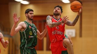 Ein Basketballspieler mit der Nummer 42 auf seinem Trikot springt, um den Ball zu werfen, während ein anderer Spieler in Grün aufmerksam zusieht.