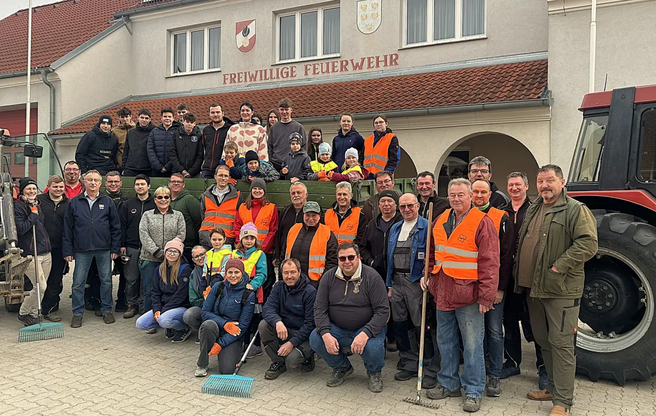Eine Gruppe von Menschen in orangewesten und Jacken posiert für ein Foto vor einem Gebäude mit dem Schild Freiwillige Feuerwehr.