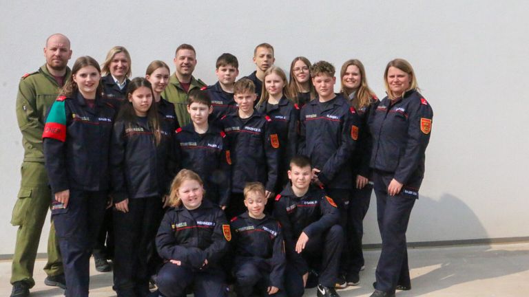 Eine Gruppe junger Menschen in passenden Uniformen posiert für ein Foto, einige stehend und einige sitzend, mit Erwachsenen in der Nähe.