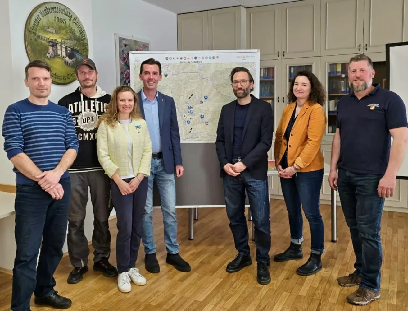 Eine Gruppe von Menschen steht in einem Raum mit einer Karte an der Wand, sie alle lächeln und scheinen für ein Foto zu posieren.