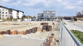 Eine Baustelle mit Haufen von Stahlrohren und einem Gebäude mit vielen Fenstern in der Ferne.