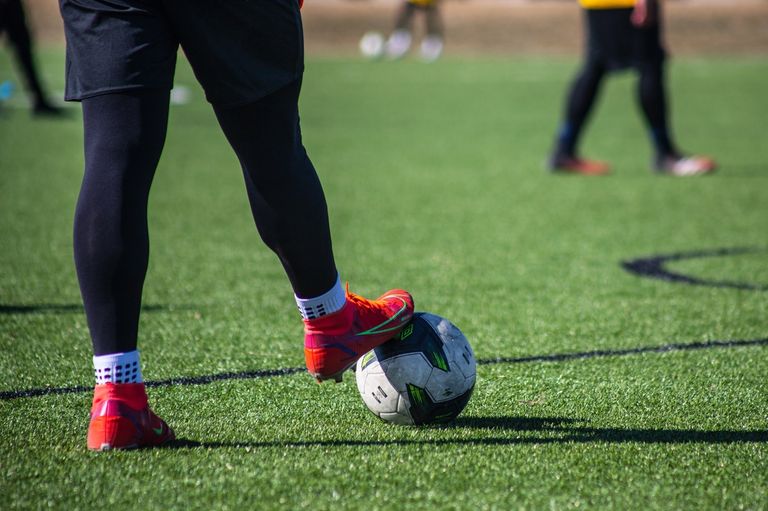 A soccer player is positioned to kick the ball with a blurred background of players in the distance.