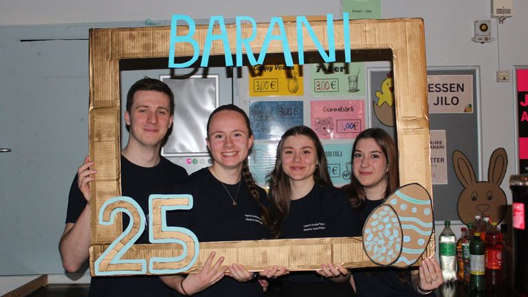 Vier junge Menschen in schwarzen T-Shirts lächeln für die Kamera in einem Pappausschnitt mit der Nummer 25 und dem Wort Barani oben.
