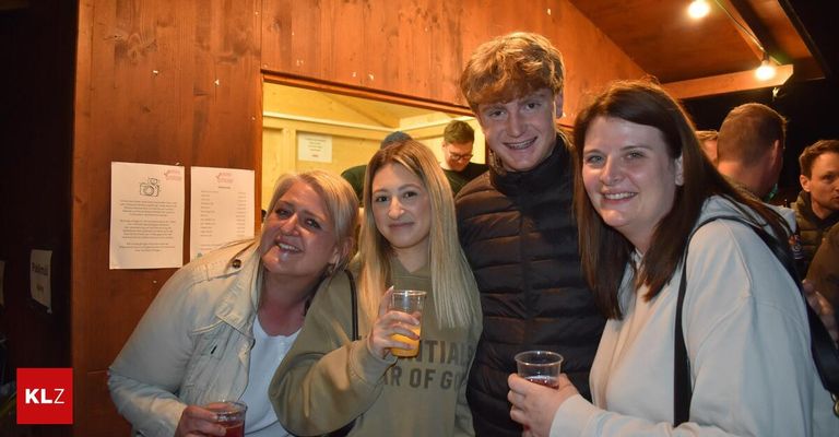 A group of four adults, two women and two men, are smiling and holding drinks inside a wooden room. The women are on the left, and the men are on the right. They are posing for a photo.