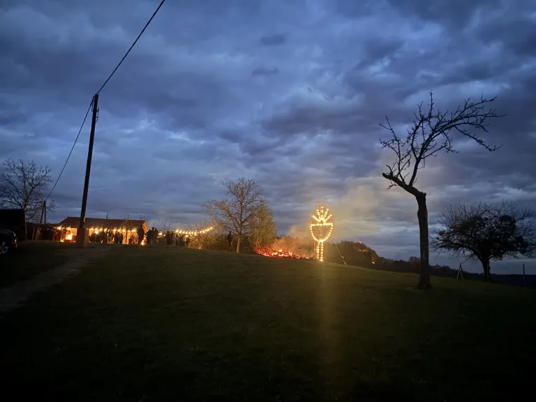 A night scene shows a hill with a bonfire in the middle and lights around it, with people gathered near a building.
