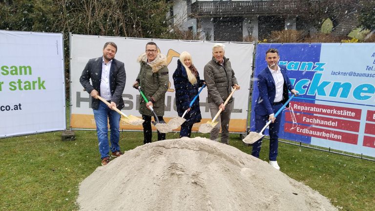 Five people shovel dirt in a snowy field. A large pile of dirt is in front of them. They are all dressed warmly.