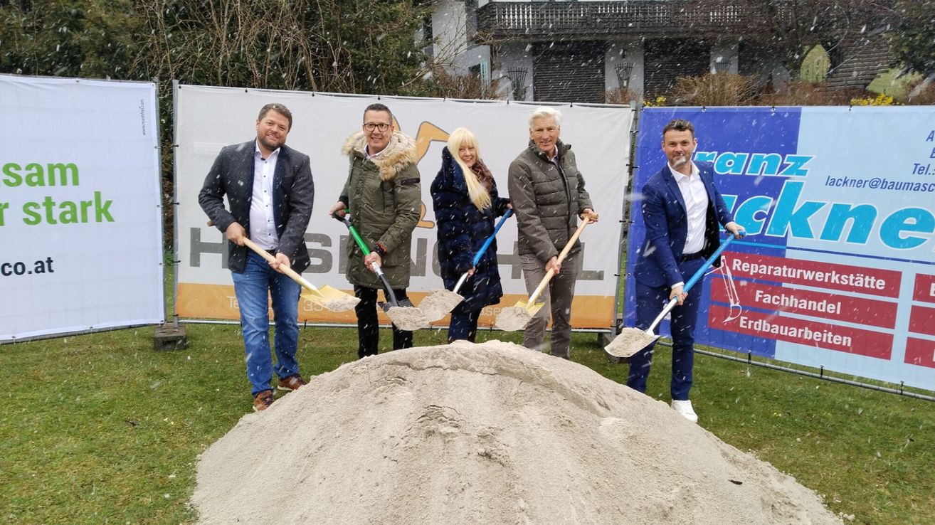 Five people shovel dirt in a snowy field. A large pile of dirt is in front of them. They are all dressed warmly.
