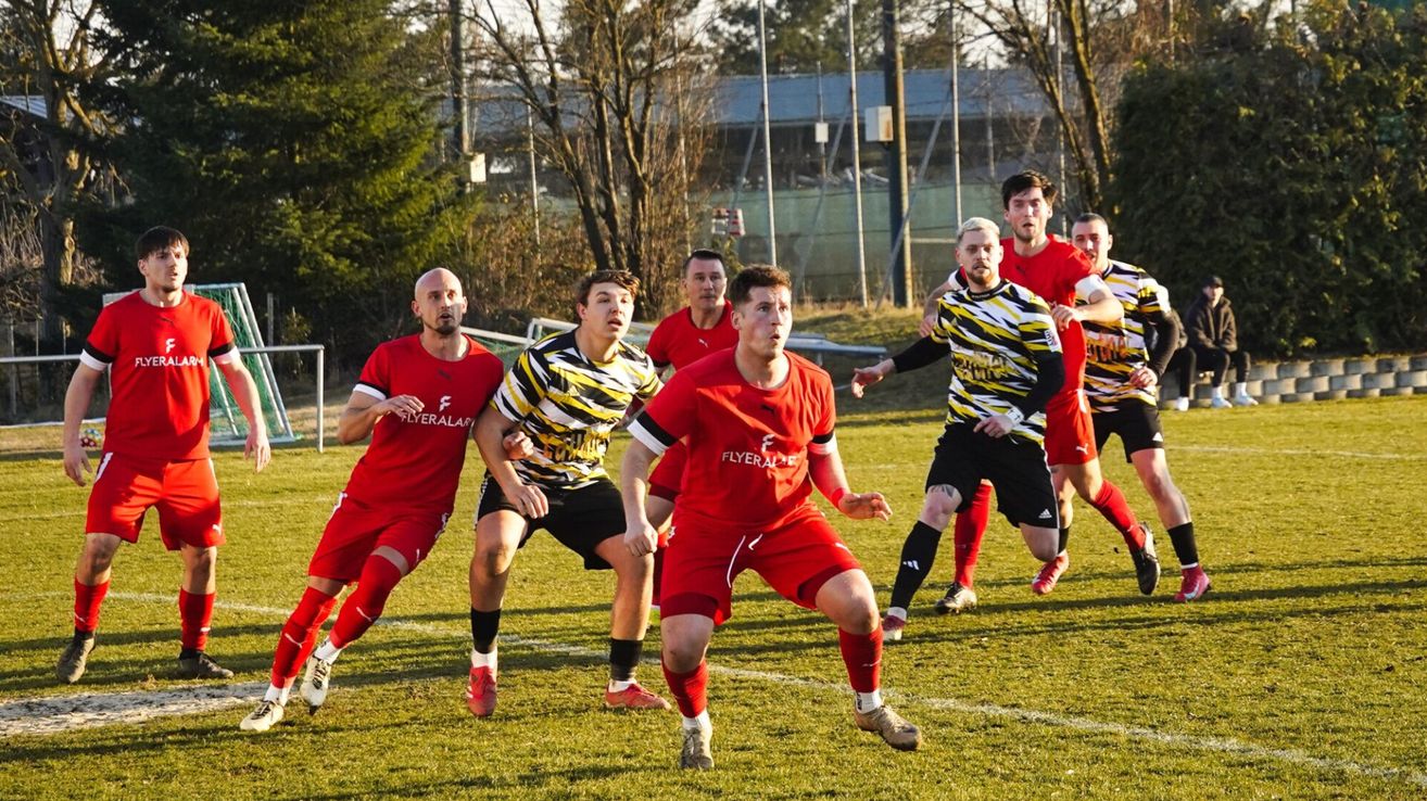 A group of men are playing soccer on a field. They are all wearing red uniforms. They are running and looking at the ball.