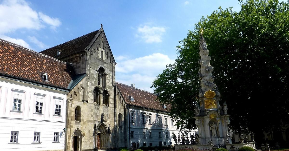 Eine historische Kirche mit kunstvollen Steinarbeiten und einem großen verzierten Brunnen davor. Das Gebäude hat ein dreieckiges Dach und Bogenfenster.