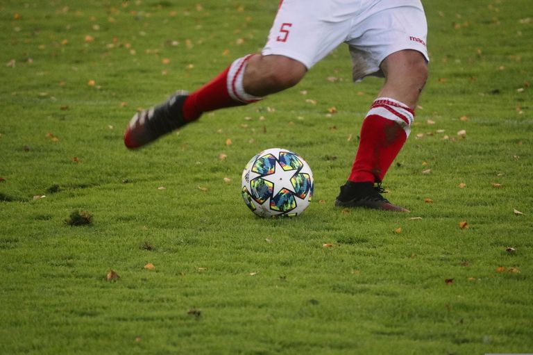 A soccer player in a white uniform with the number 5 kicks a soccer ball on a grassy field.