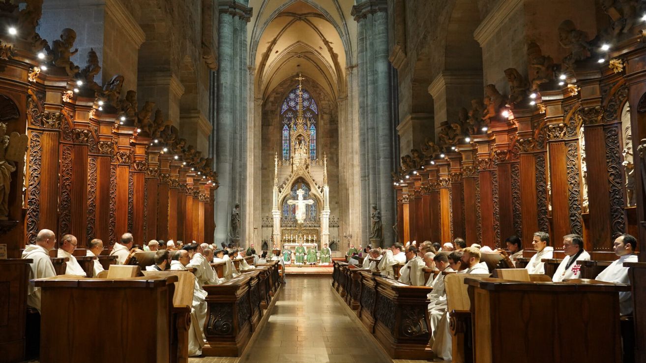 Eine Gruppe von Menschen in weißen Gewändern sitzt in einer Kirche und schaut auf den Altar mit einem großen Kreuz.