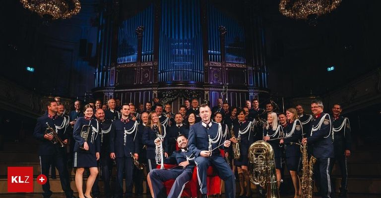 A group of musicians in uniform poses for a photo with their instruments in front of a blue pipe organ.