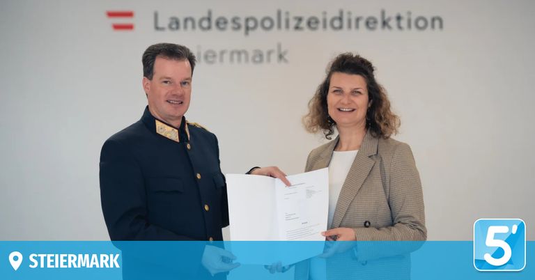 Ein Mann und eine Frau in formeller Kleidung halten ein Papier vor einem weißen Hintergrund mit dem Text Landespolizeiinspektion.