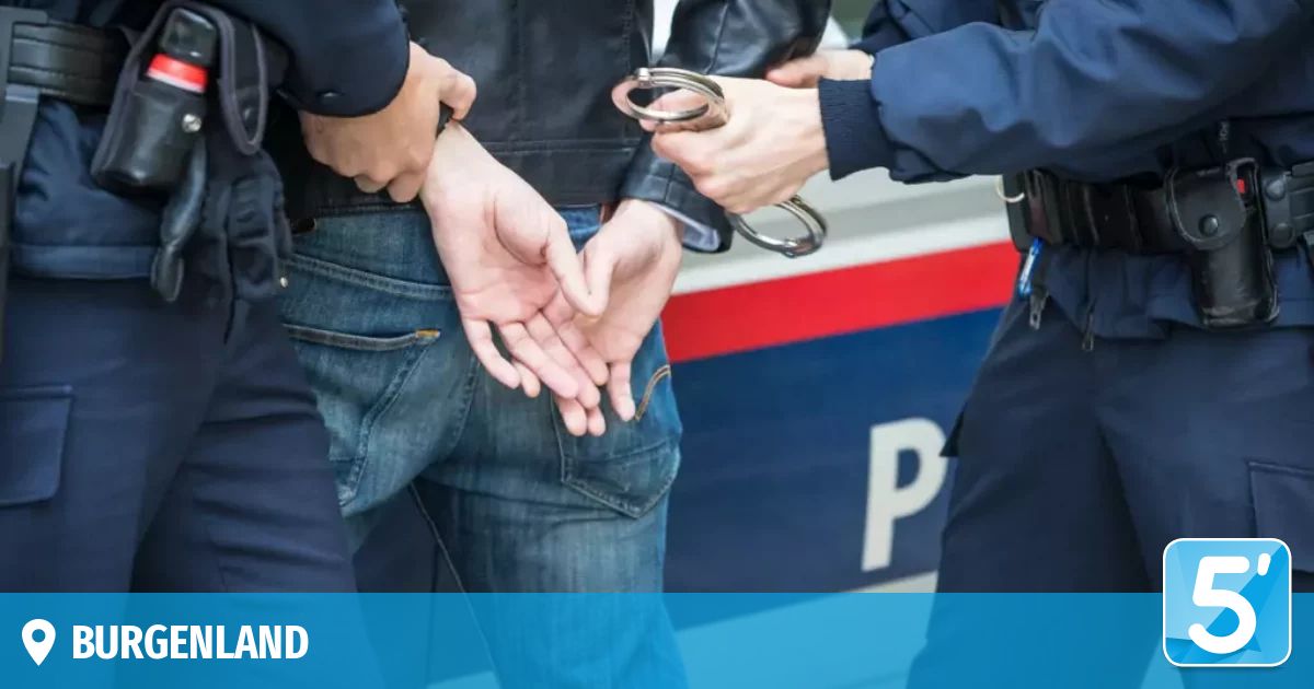 Three police officers in uniform are detaining a man with handcuffs in front of a police car.