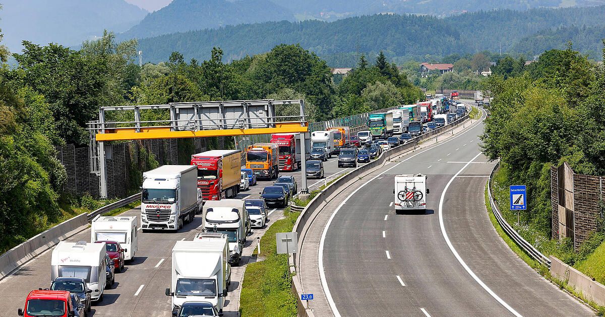 A highway with many trucks and cars stuck in a traffic jam. Trees and mountains are in the background.
