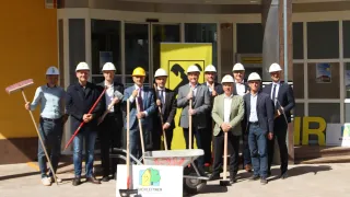 A group of men in construction gear and suits stand in front of a building with shovels. The banner behind them has a cartoon character and the text 'Duchleitner.'