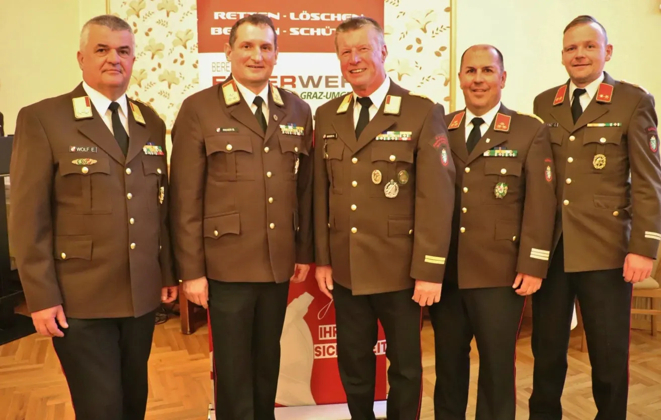 Four military officers in brown uniforms and medals pose for a photo in front of a banner.
