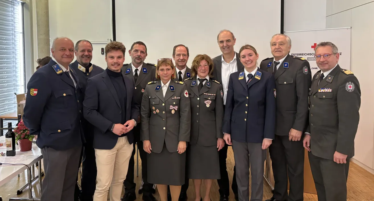 A group of military officers and soldiers standing together for a photograph, with two women in front wearing medals and one woman holding a red cross emblem.