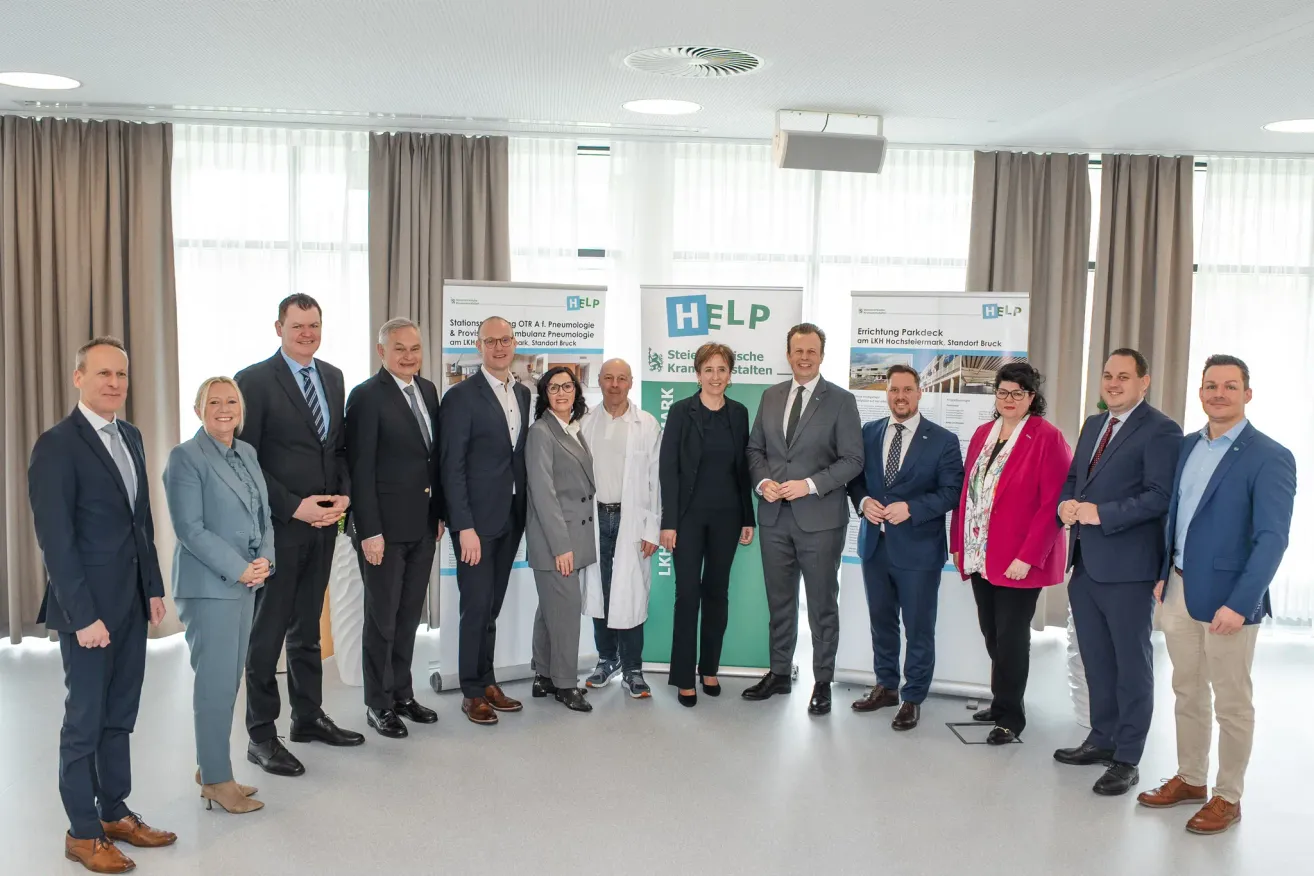 Several people in suits and ties pose for a picture in a conference room, with banners and curtains in the background.