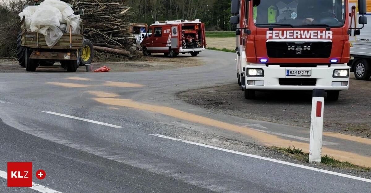 A fire truck is parked on the side of the road with a pile of firewood and a white car in the background.
