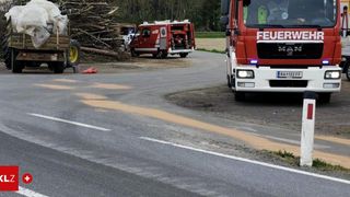 A fire truck is parked on the side of the road with a pile of firewood and a white car in the background.