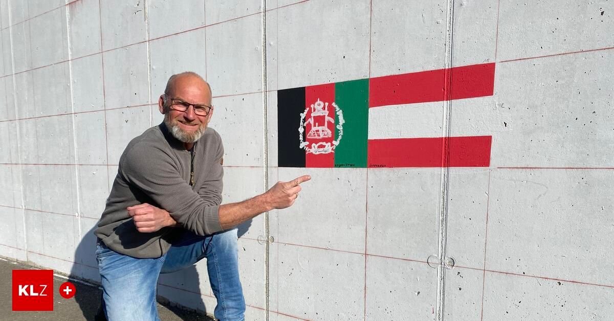 A man pointing to a mural of the Afghan flag on a concrete wall.