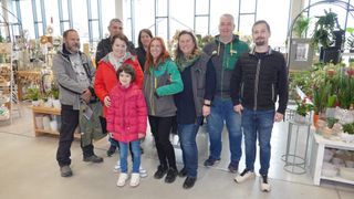 A group of people, including men, women, and a child, are standing together in a room with glass walls, smiling for a photo.