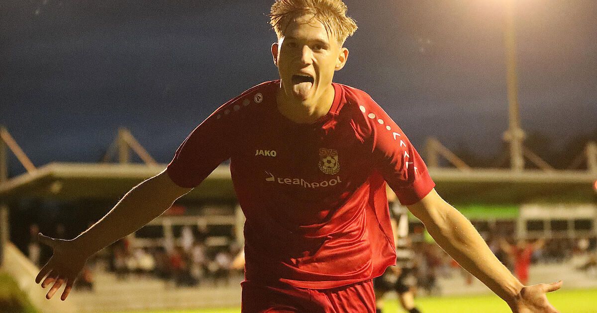 A soccer player in a red jersey celebrates a goal on the field at night.