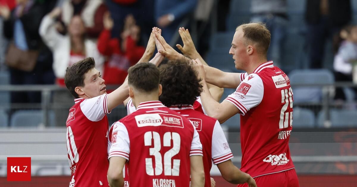 A group of young soccer players in red and white uniforms are celebrating with their hands together. Player number 32 is looking to the side.