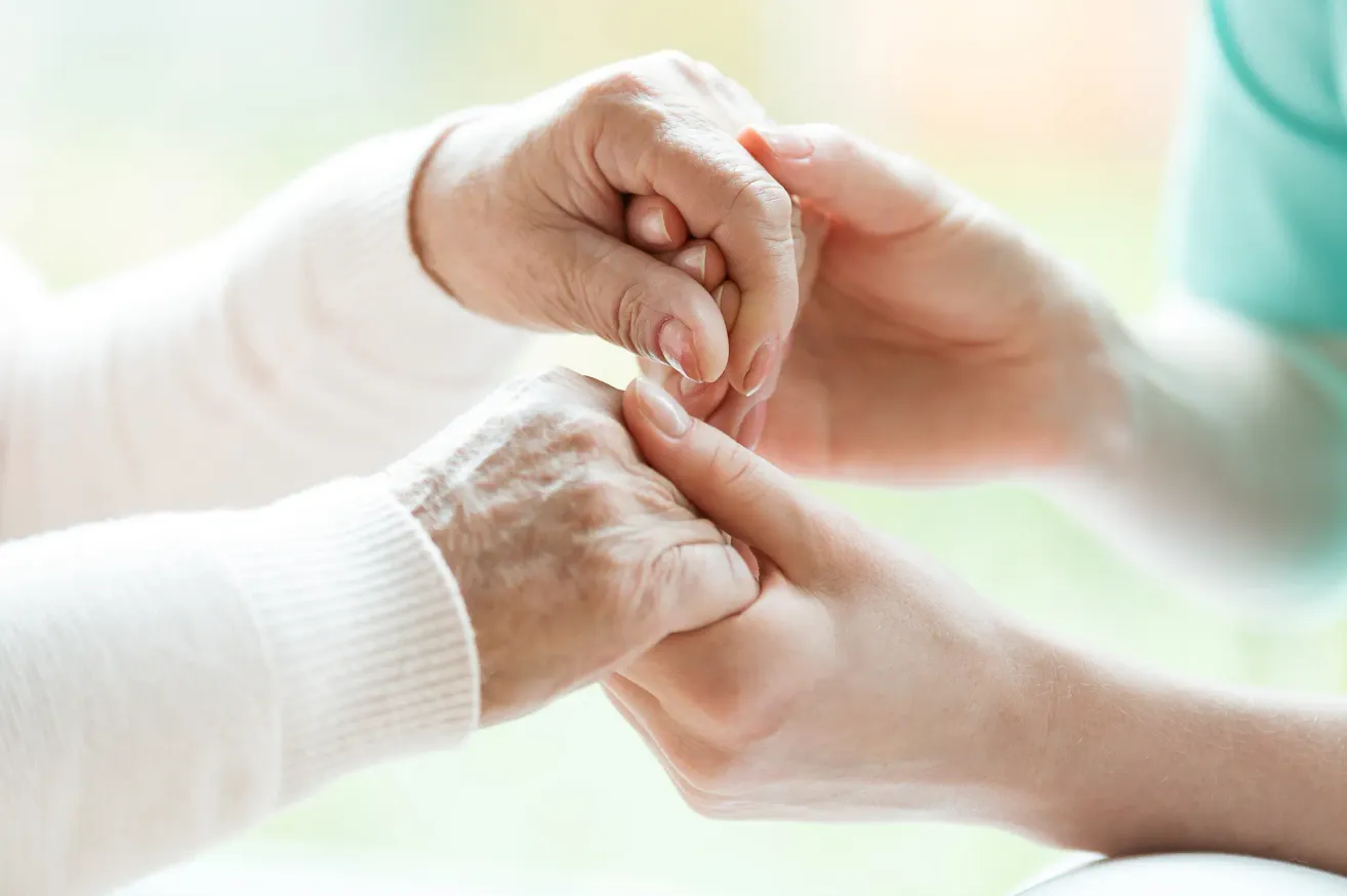 An elderly person's hand is being held by another hand, possibly a family member or caregiver, showing support and care.