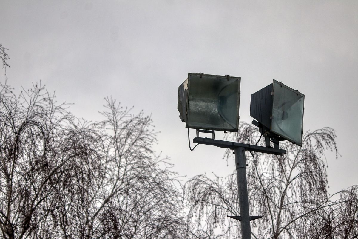 Two streetlights mounted on a pole with glass covers. The sky is overcast, and bare trees are in the background.
