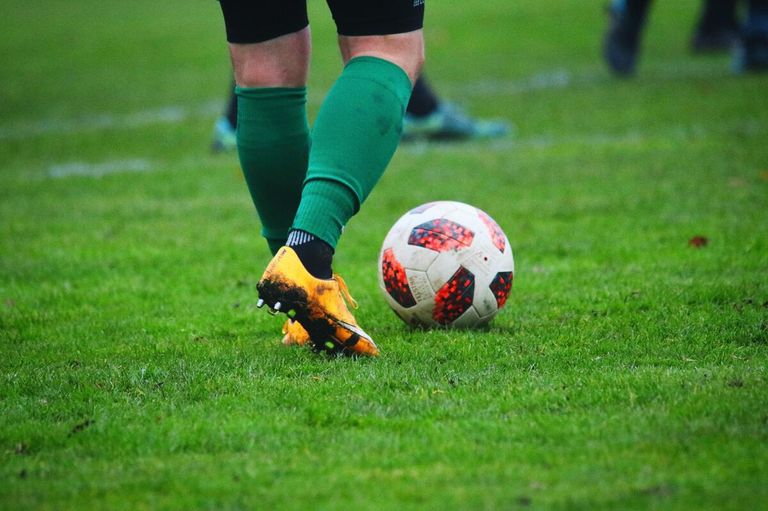 A soccer player in green socks and yellow cleats is about to kick a soccer ball on a field.