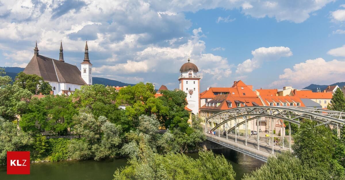 A town with a bridge, buildings, and a clock tower under a cloudy sky.