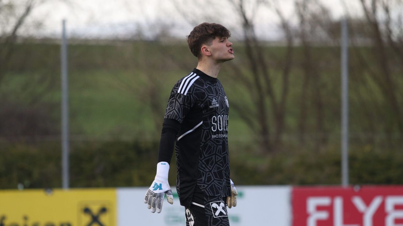 A soccer goalkeeper in a black jersey with the word 'SOUL' and Adidas logo on it, looking upwards.