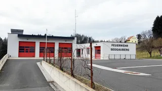 The Segganberg fire station has red garage doors and a white wall with a fence in front.