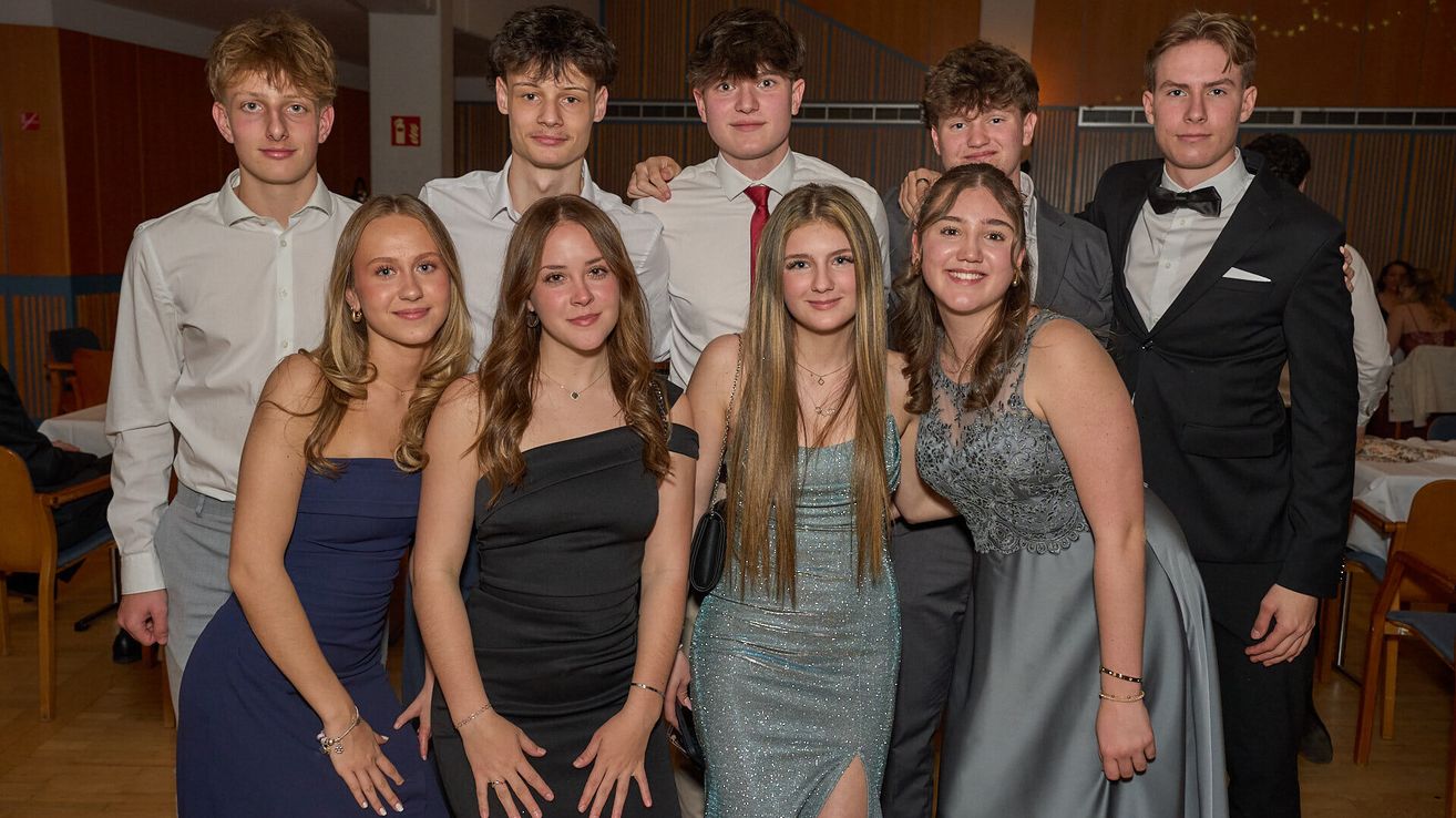 A group of young adults, both male and female, are posing for a photograph at a formal event. They are all smiling and dressed in formal attire.