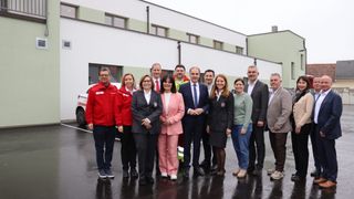 A group of individuals, including emergency personnel and officials, stand together in front of a building, likely for a group photo.