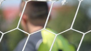 A soccer player's back with a number 1 jersey, standing behind a net, blurred background.