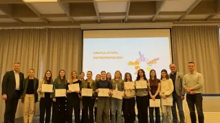 A group of women and men are standing on a stage holding certificates. They are posing for a photo in front of a projector screen.