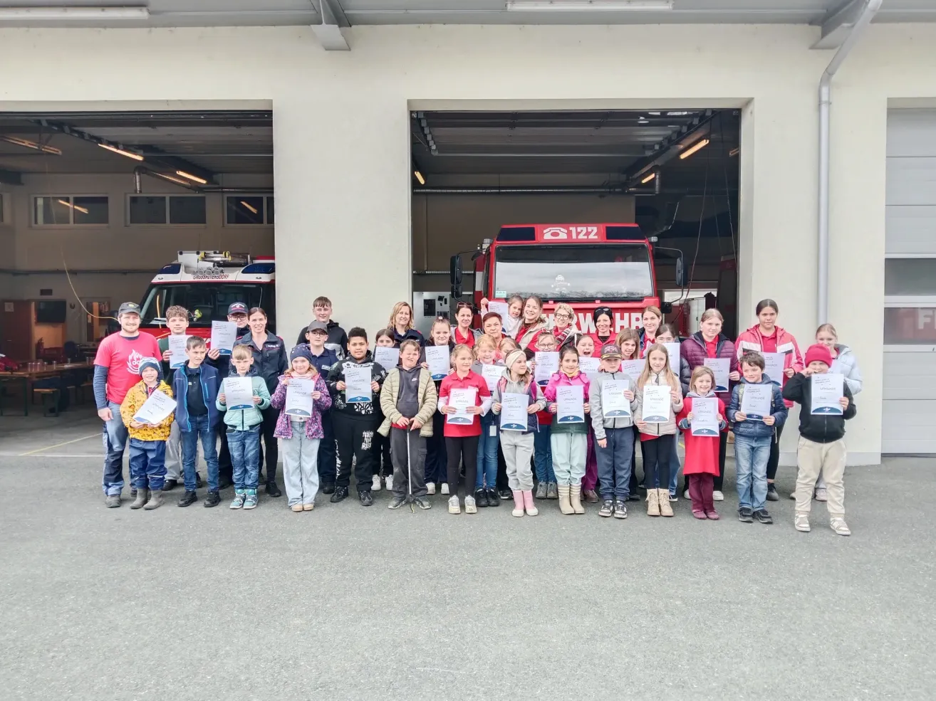 A group of children and adults stands in front of a fire truck. They are all holding certificates and smiling for a photo.