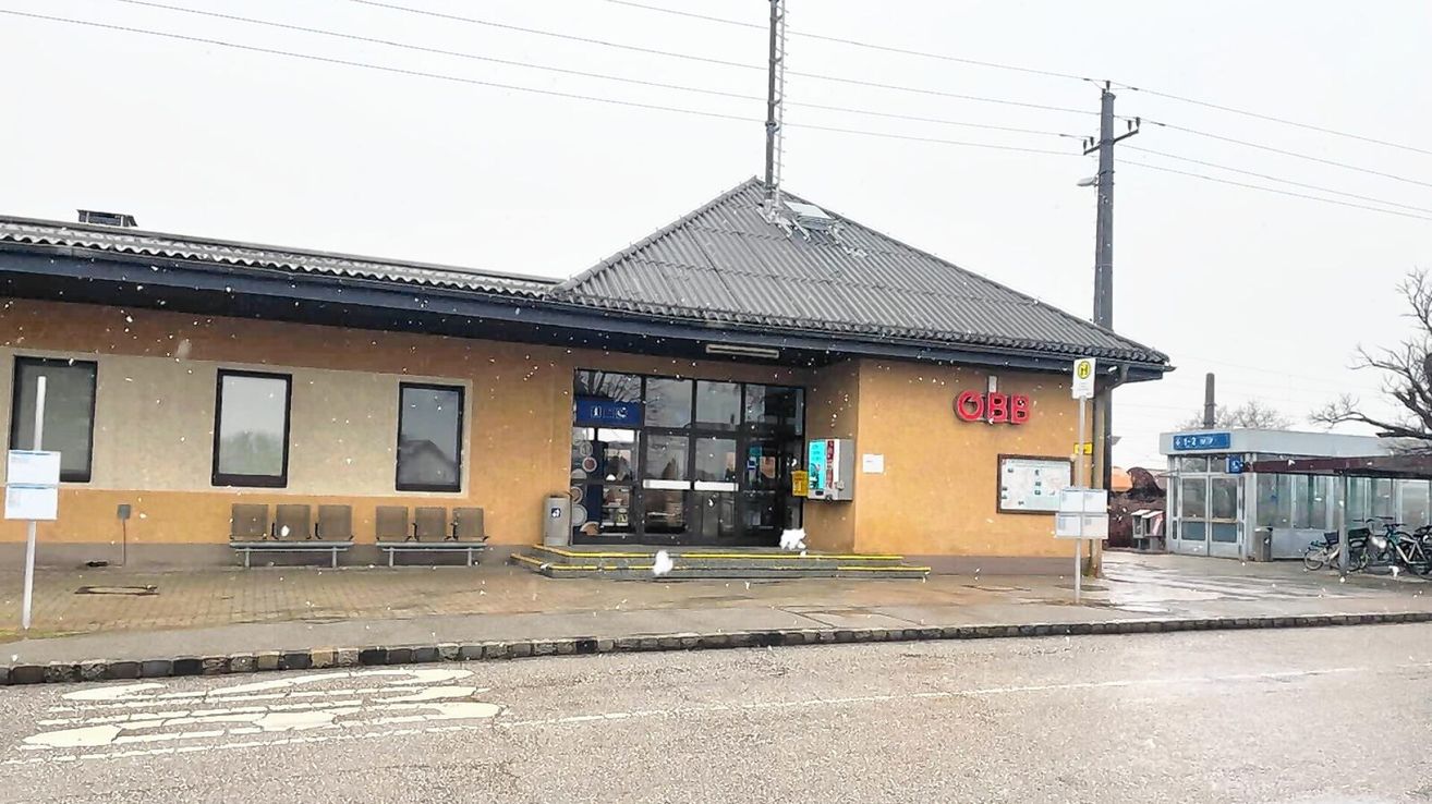 A small building with a flat roof has a sign that reads OBB. It has a glass entrance and three benches outside.