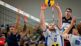 A man in a volleyball jersey with number 13 is playing volleyball and trying to block the ball. Another player is trying to hit the ball.
