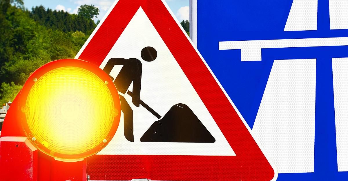 Ein Verkehrsschild warnt vor bevorstehenden Straßenarbeiten mit einer Silhouette eines Arbeiters und einer gelben Leuchte.