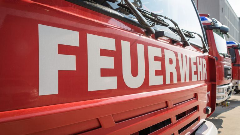 Ein Nahaufnahme eines roten Fahrzeugs mit dem Wort 'FEUERW' prominent in Weiß dargestellt. Das Fahrzeug ist wahrscheinlich ein Feuerwehrwagen.