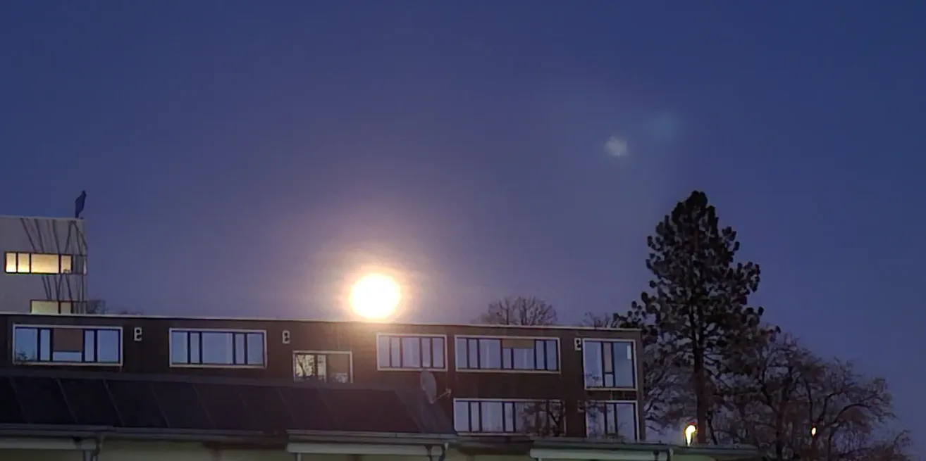 Ein Gebäude mit einem Solarpanel auf dem Dach ist bei Nachthimmel sichtbar, während die Sonne in der Ferne hell scheint.